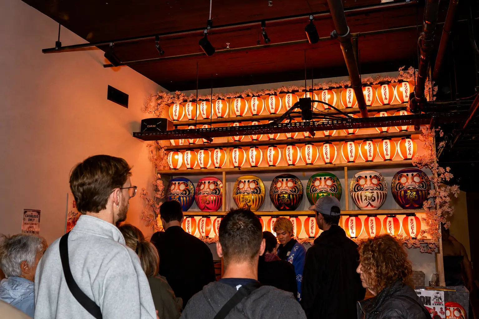 Guests arriving beneath glowing lanterns and colorful daruma displays